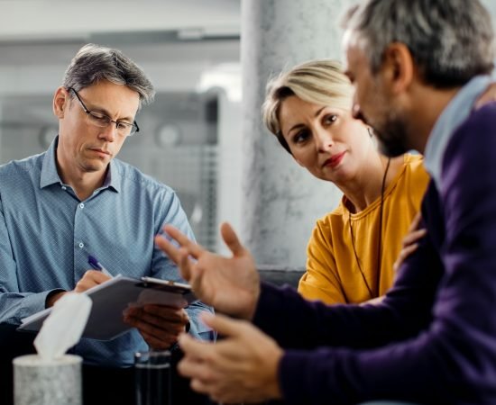 Marriage counselor taking notes while having meeting with a couple in the office.